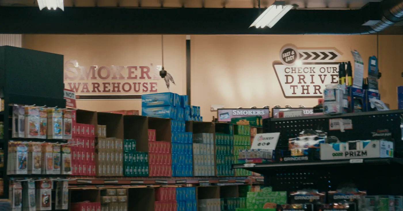 The Smoker's Warehouse sign on the back wall above shelves of cartons and pouches
