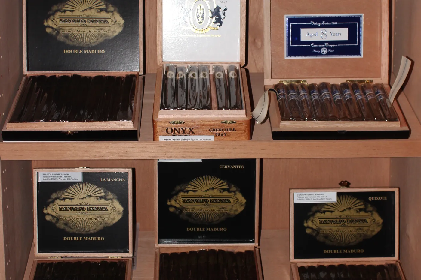 Open cigar boxes angled on the humidor shelves, lids up so the bands are visible
